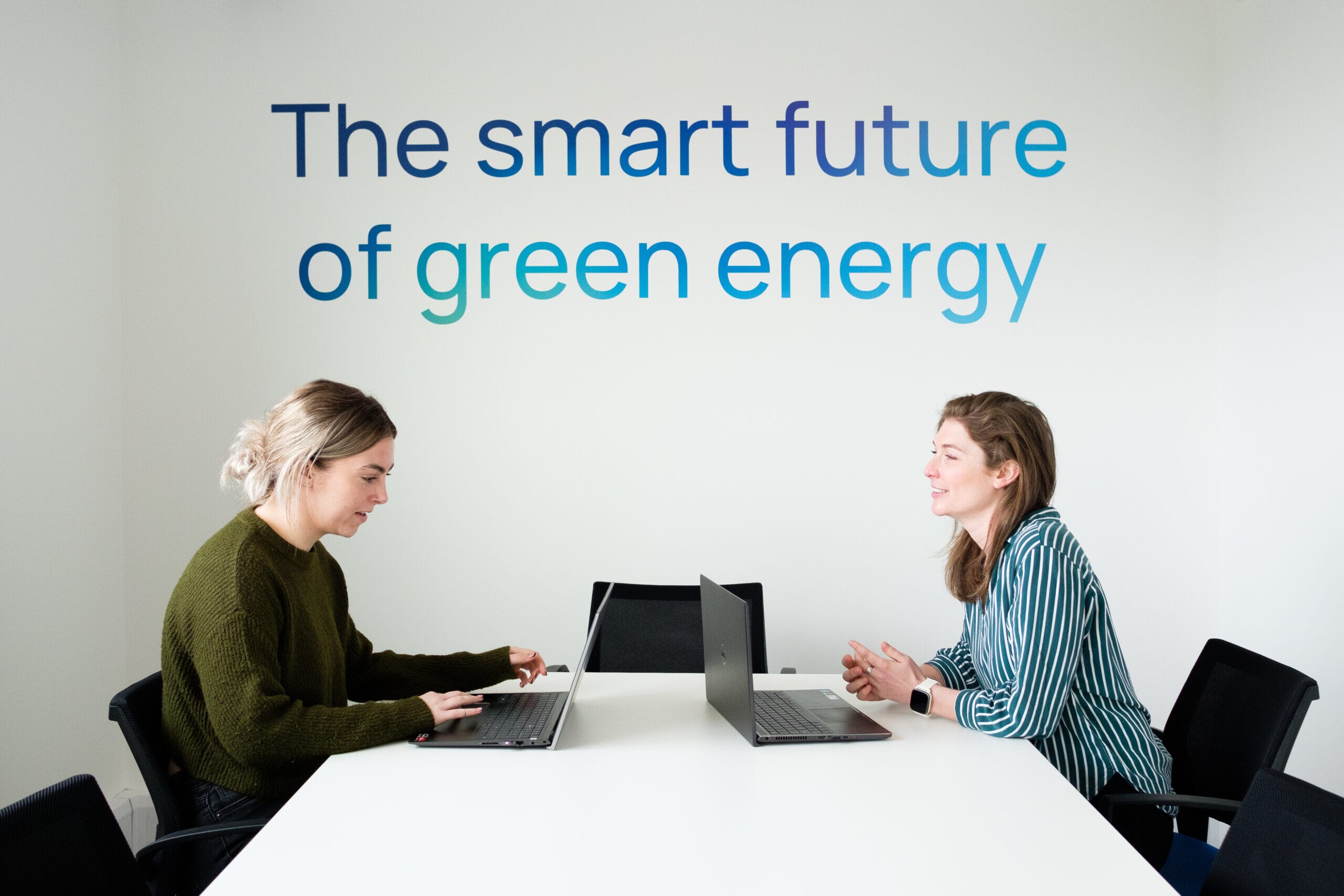 Two women sitting at a meeting room table with laptops beneath the Innova tagline "The smart future of green energy."